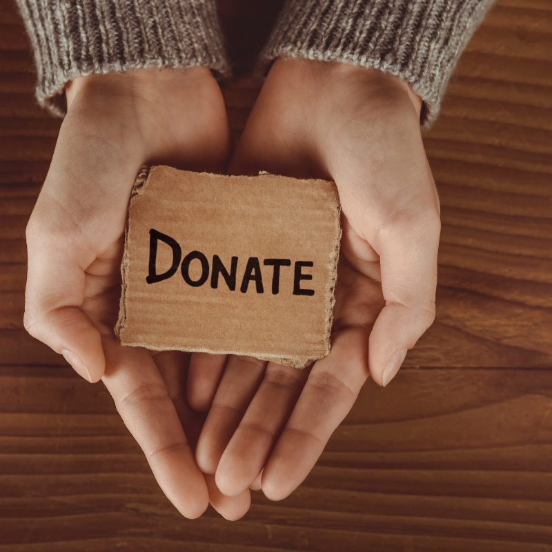 The photo shows a pair of hands holding a small card that says "Donate."